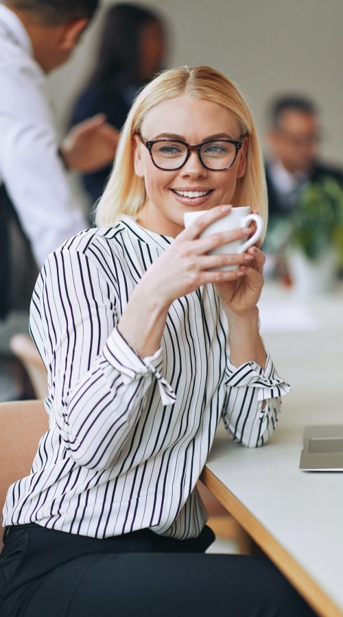 smiling-young-businesswoman-sitting-at-work-drinking-a-coffee.jpg